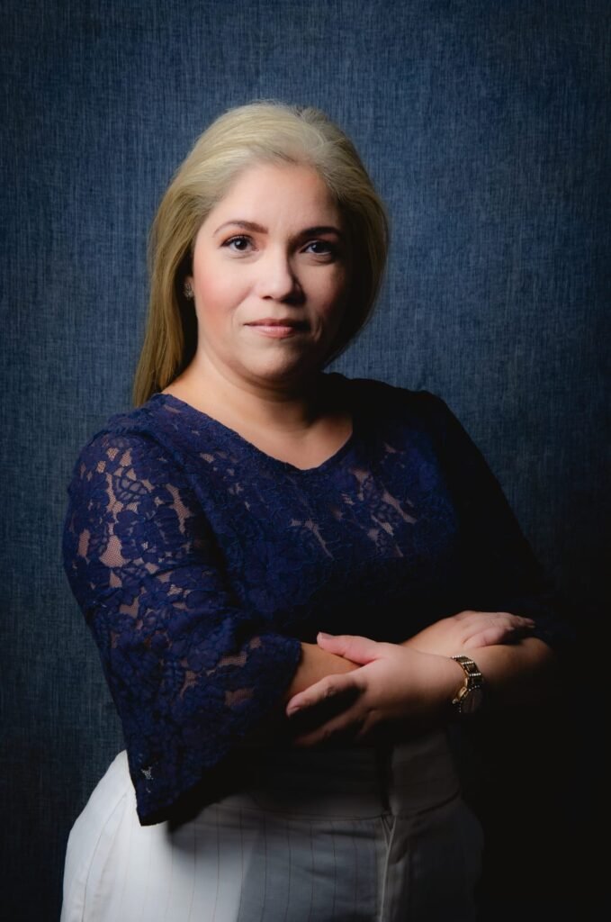 Advogada Fabiola Carneiro com uma blusa de manga longa azul marinho, posando para a foto num fundo azul escuro